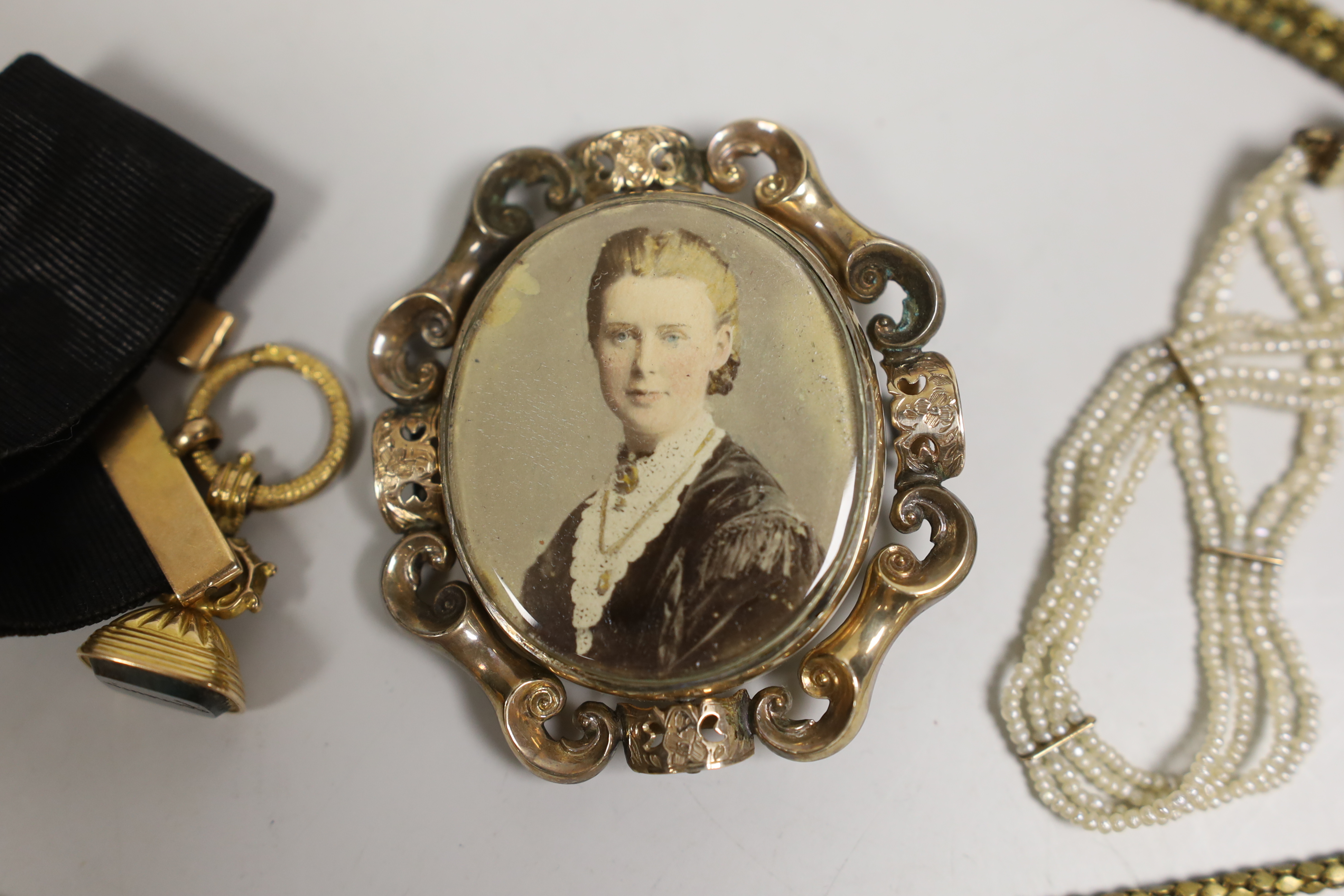 A 19th century yellow metal overlaid and bloodstone set fob seal, 22mm, on a yellow metal mounted black sash, a similar gilt metal guard chain and mourning pendant and a Regency seed pearl bracelet.